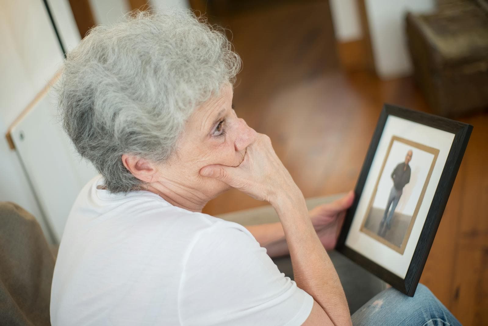 A thoughtful elderly woman with a framed family photo — the small moments of memory care at home.